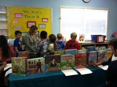 2nd graders with their teacher, Claudia Lewis, considering which books they want to check out first.